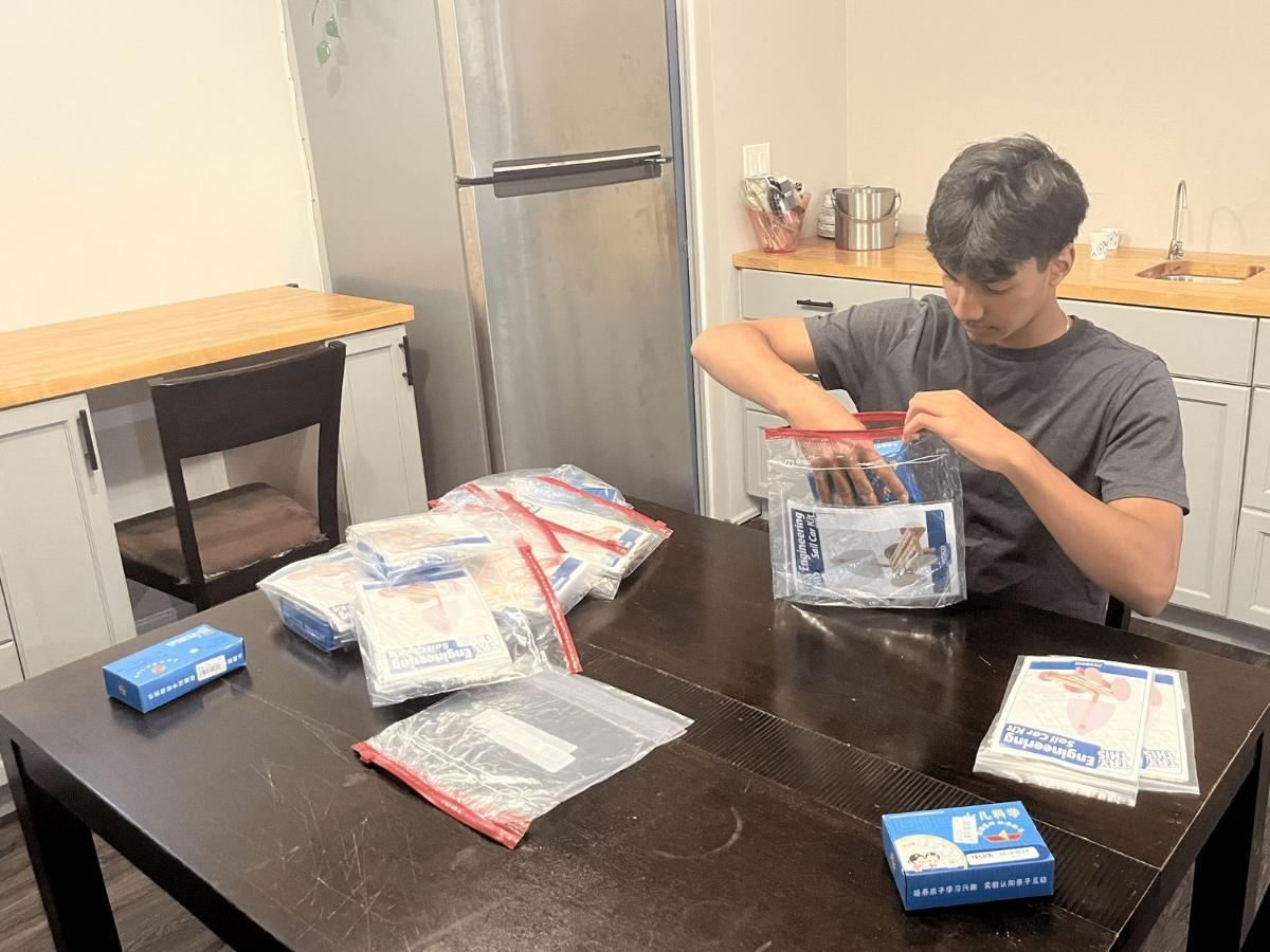 A Future Spark student sealing a kit at a kitchen table with a stack of finished kits beside him